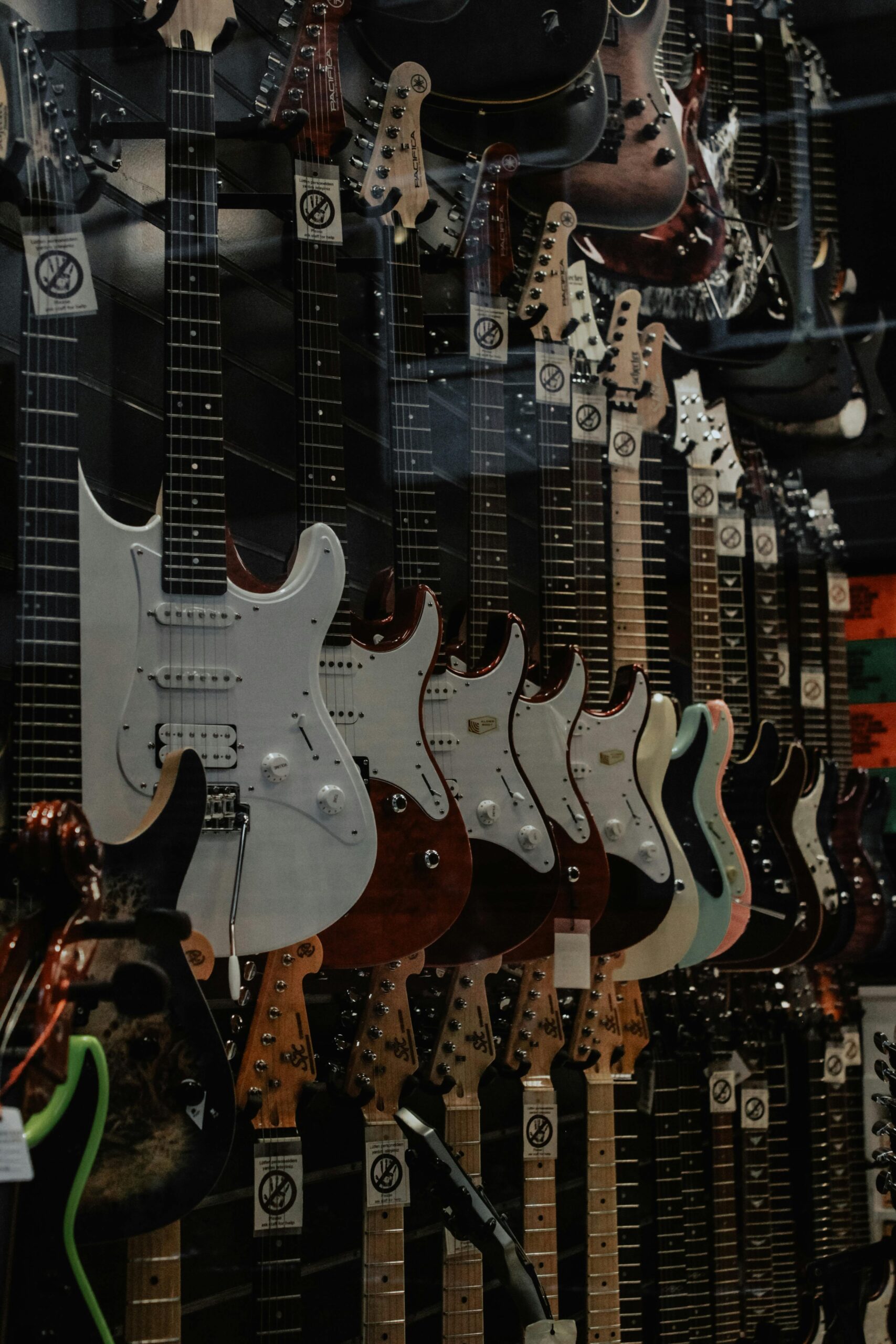 A vertical shot of assorted electric guitars hanging on a wall display in a music store.