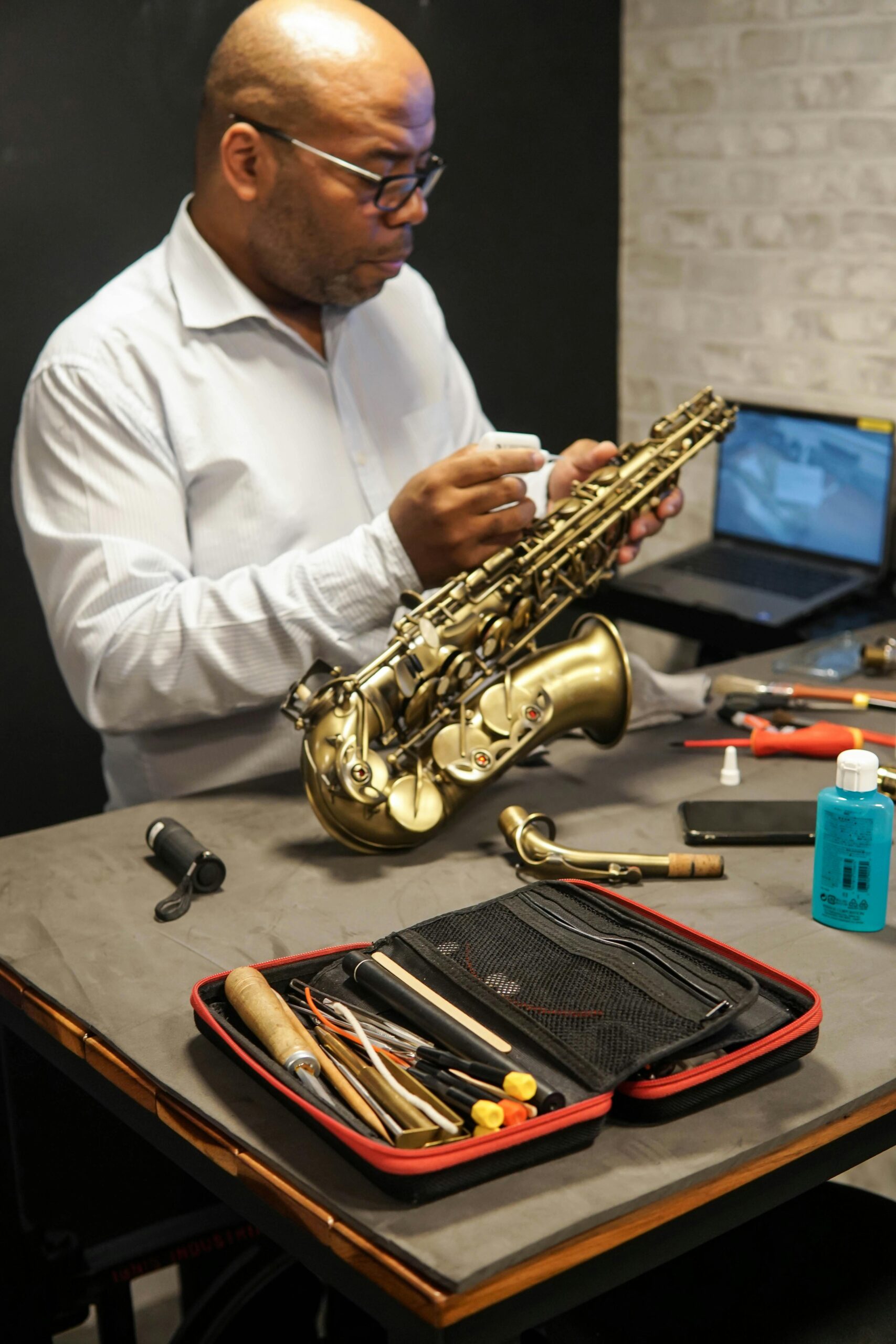 A skilled technician carefully repairs a saxophone, surrounded by tools, indoors.