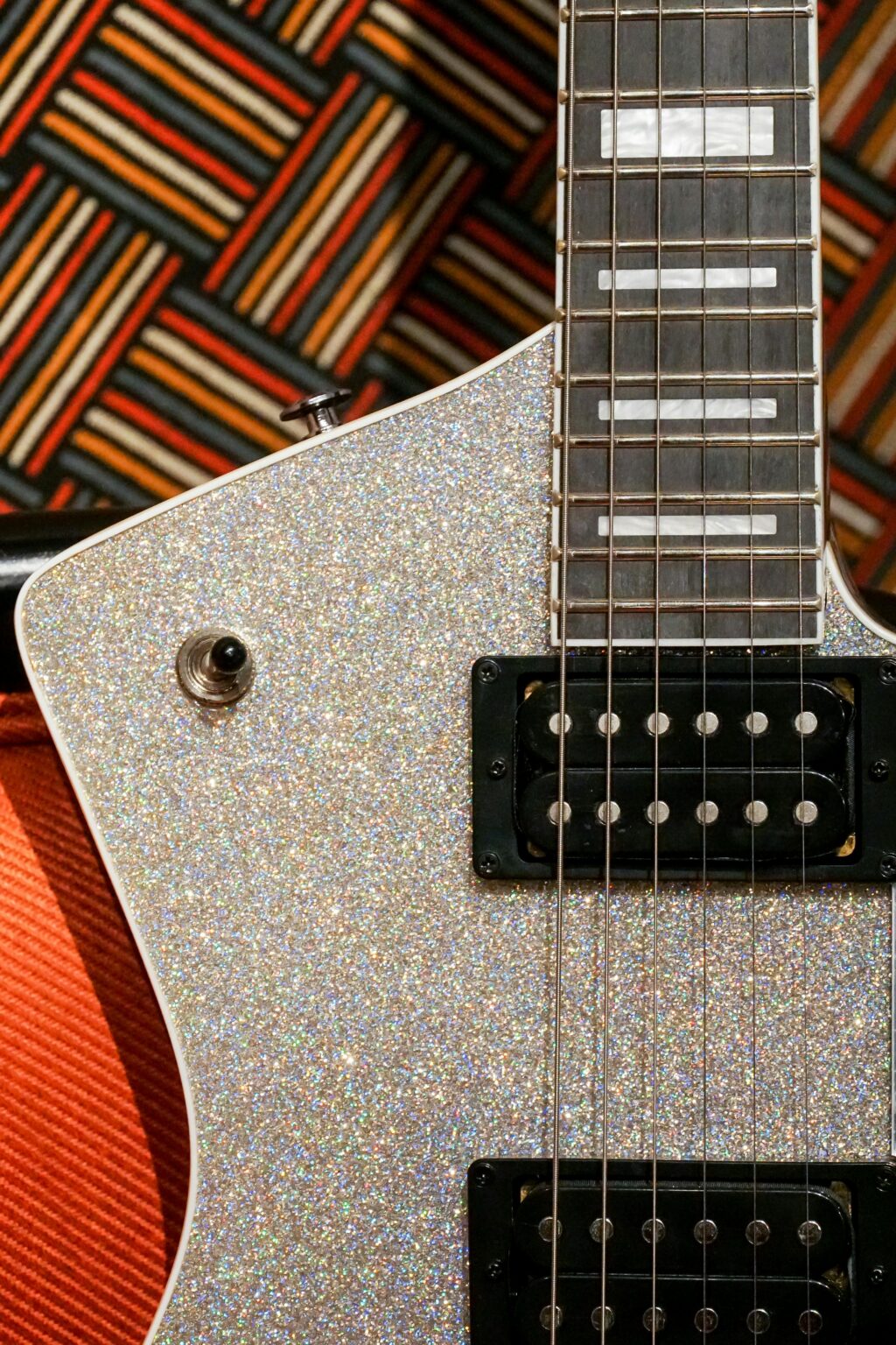 Close-up of a sparkling electric guitar with a geometric patterned background, highlighting musical style.