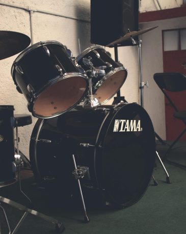 Black drum set in a music rehearsal room, featuring a Tama bass drum.